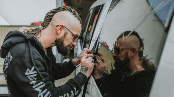 A man with dreadlocks applies tint to a vehicle window, focused and precise. - Photo by Helena Jankovičová Kováčová on Pexels