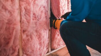 Crop unrecognizable worker in gloves sitting on haunches and insulating with pink stone wool - Photo by Erik Mclean on Pexels