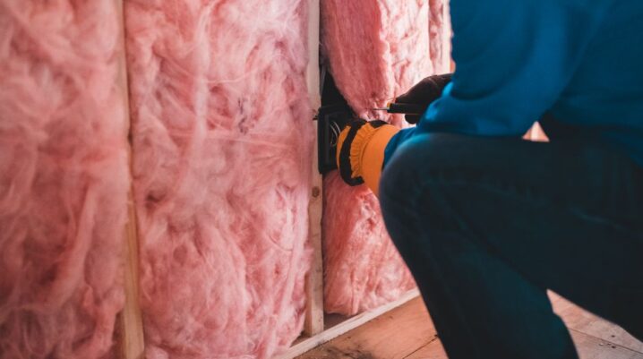 Crop unrecognizable worker in gloves sitting on haunches and insulating with pink stone wool - Photo by Erik Mclean on Pexels