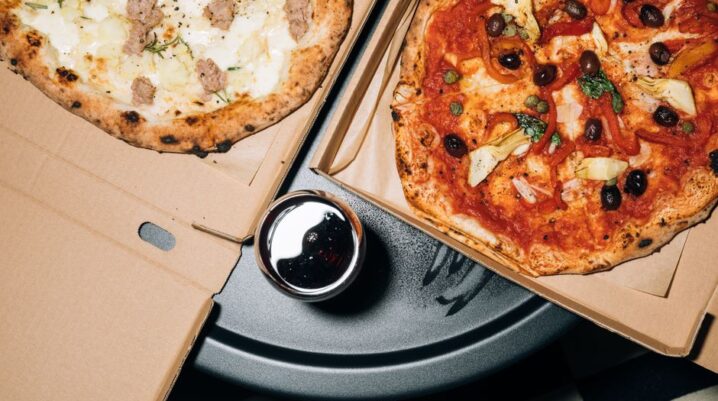 Top view of delicious pizzas in boxes with a refreshing drink, perfect for a cozy meal. - Photo by KoolShooters on Pexels